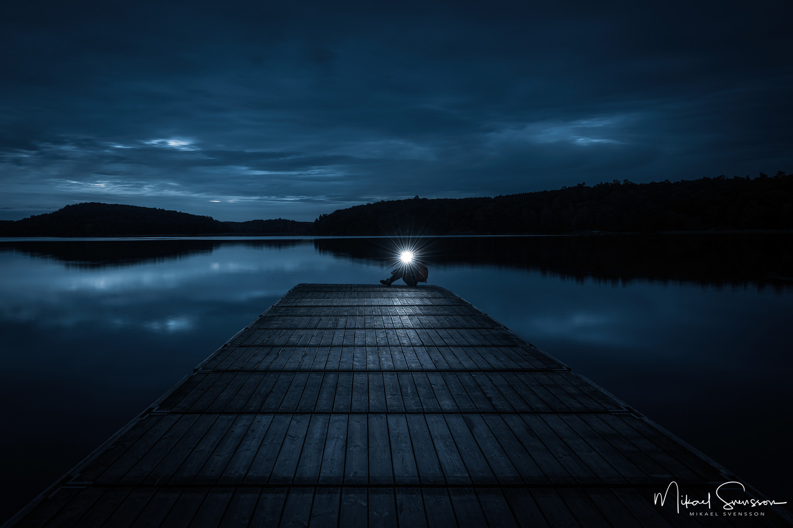Man sitter på brygga med pannlampa. Rådasjön, Mölndal.