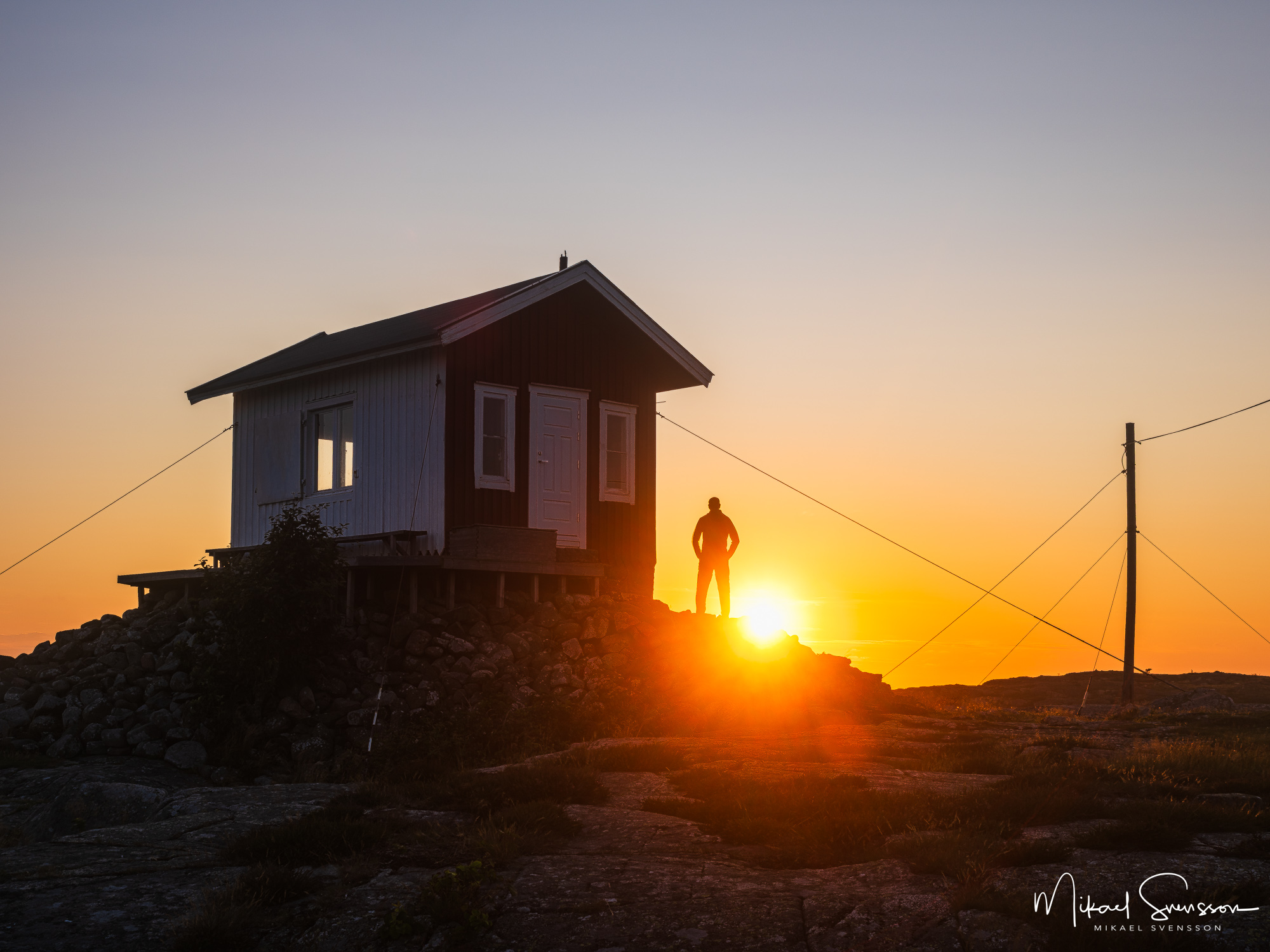 Silhuett av människa vid lotshus i solnedgång. Mönster, Kungsbacka kommun.